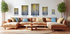 a modern living room with a large sectional sofa, a coffee table, and several framed paintings of trees on the wall.