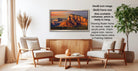 a living room with a large framed landscape photograph hanging on the wall. The photograph depicts a scenic mountain landscape with a sunset. The room is furnished with two chairs and a coffee table, creating a cozy and inviting atmosphere.