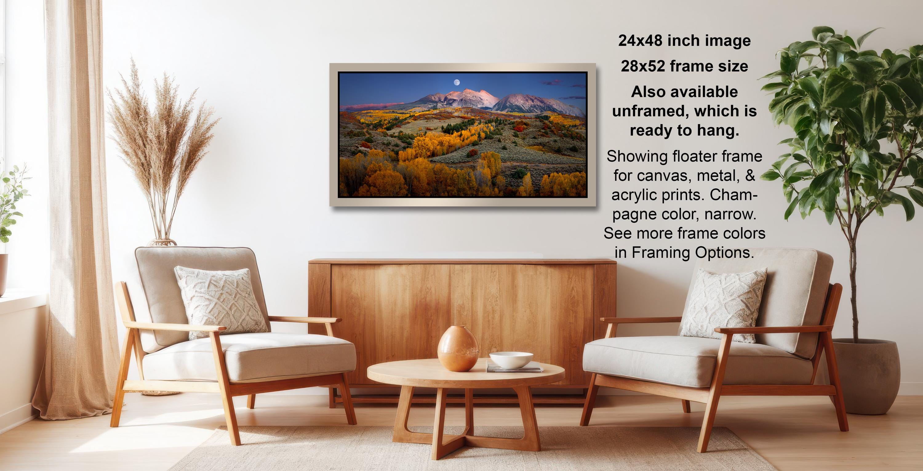 a living room with a large framed landscape painting hanging on the wall. The painting depicts a mountainous landscape with a full moon in the sky. The room is furnished with two chairs and a coffee table, creating a cozy and inviting atmosphere.