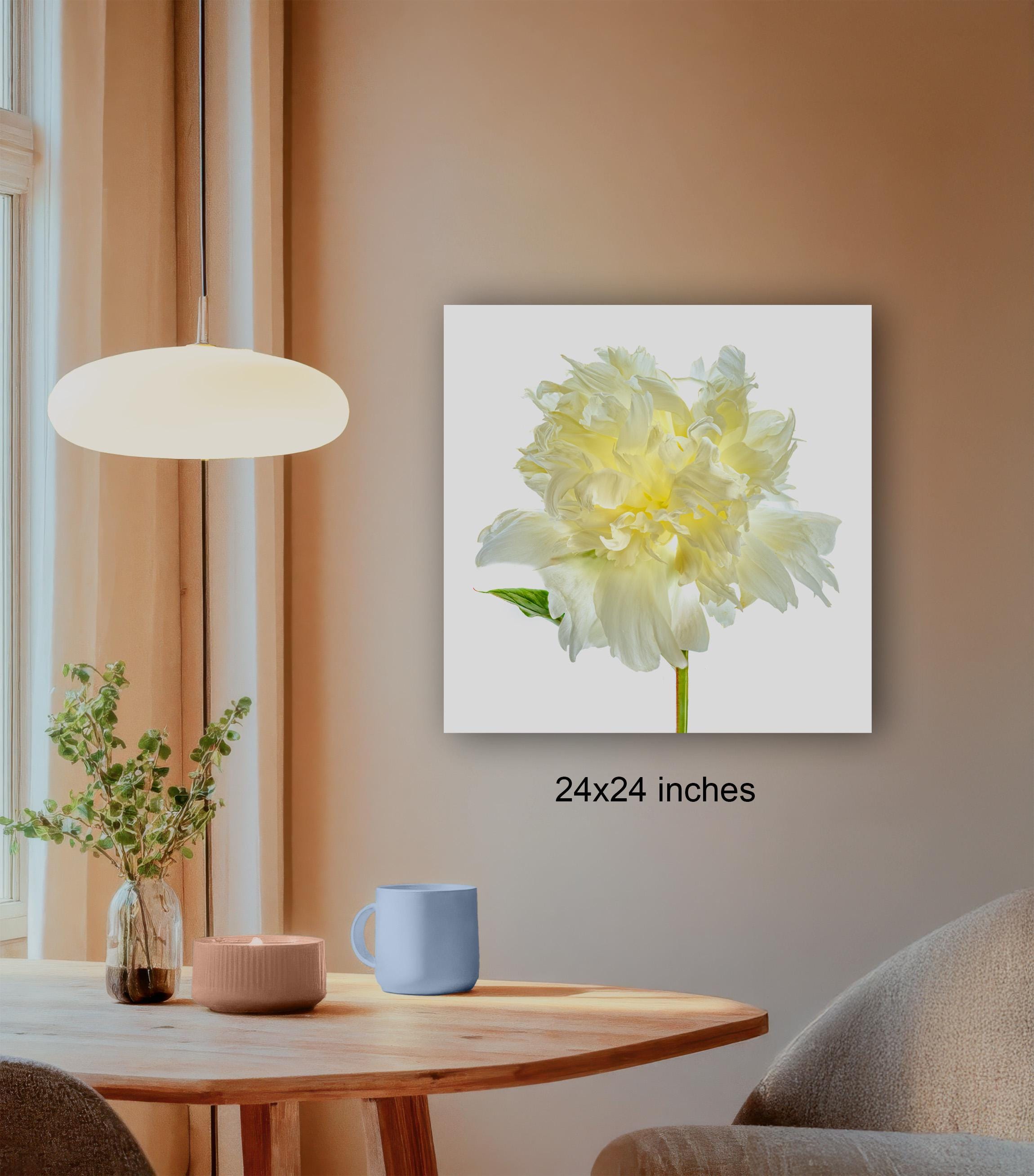 a wooden table with a blue mug, a candle, and a plant, set against a beige wall with a framed photograph of a yellow flower hanging above it.