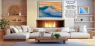 a cozy living room with a fireplace, white sofas, and a coffee table. The room has a warm and inviting atmosphere, with a large framed picture of a crashing wave hanging on the wall.