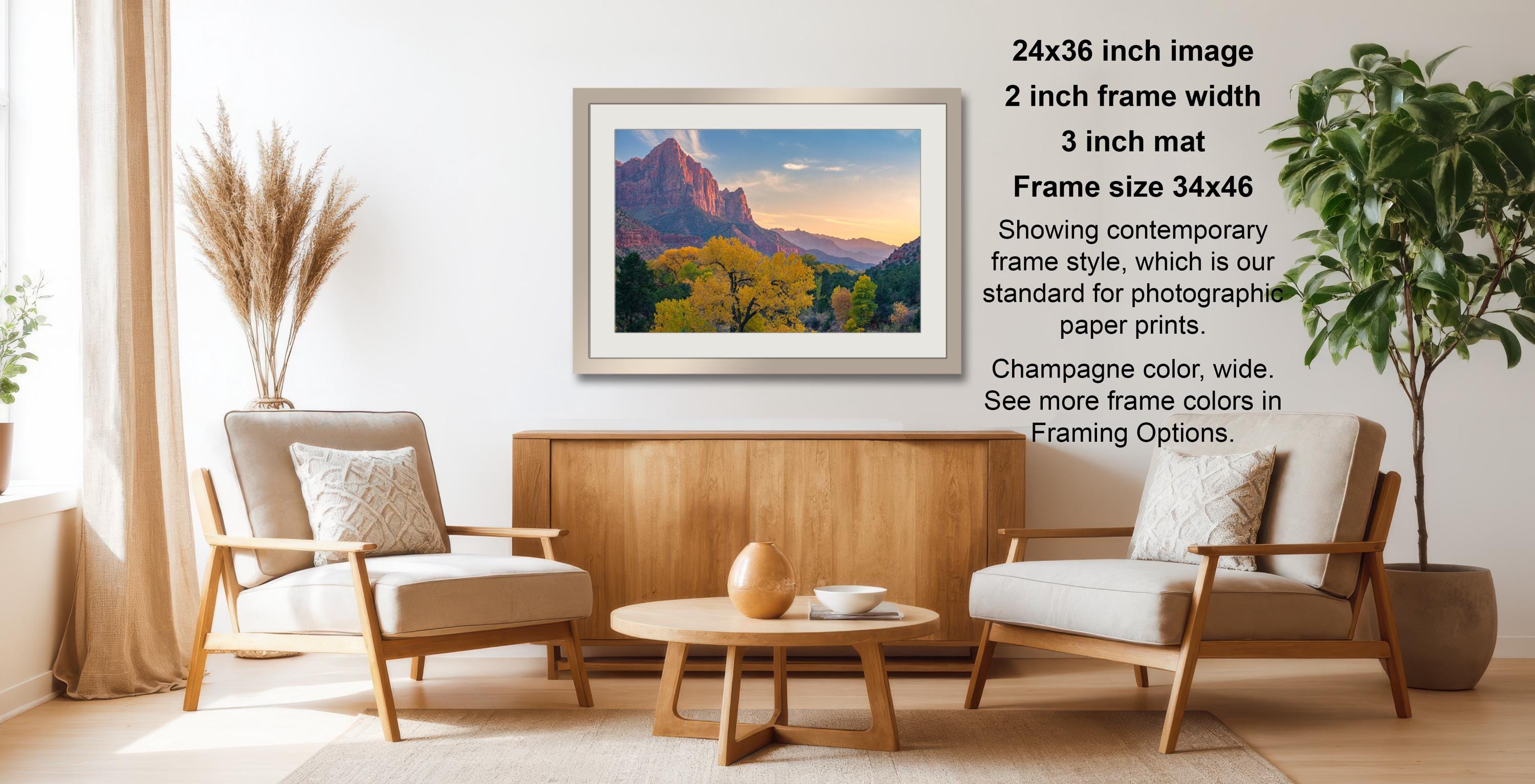 a living room with a wooden coffee table, two white armchairs, and a framed landscape photograph hanging on the wall.