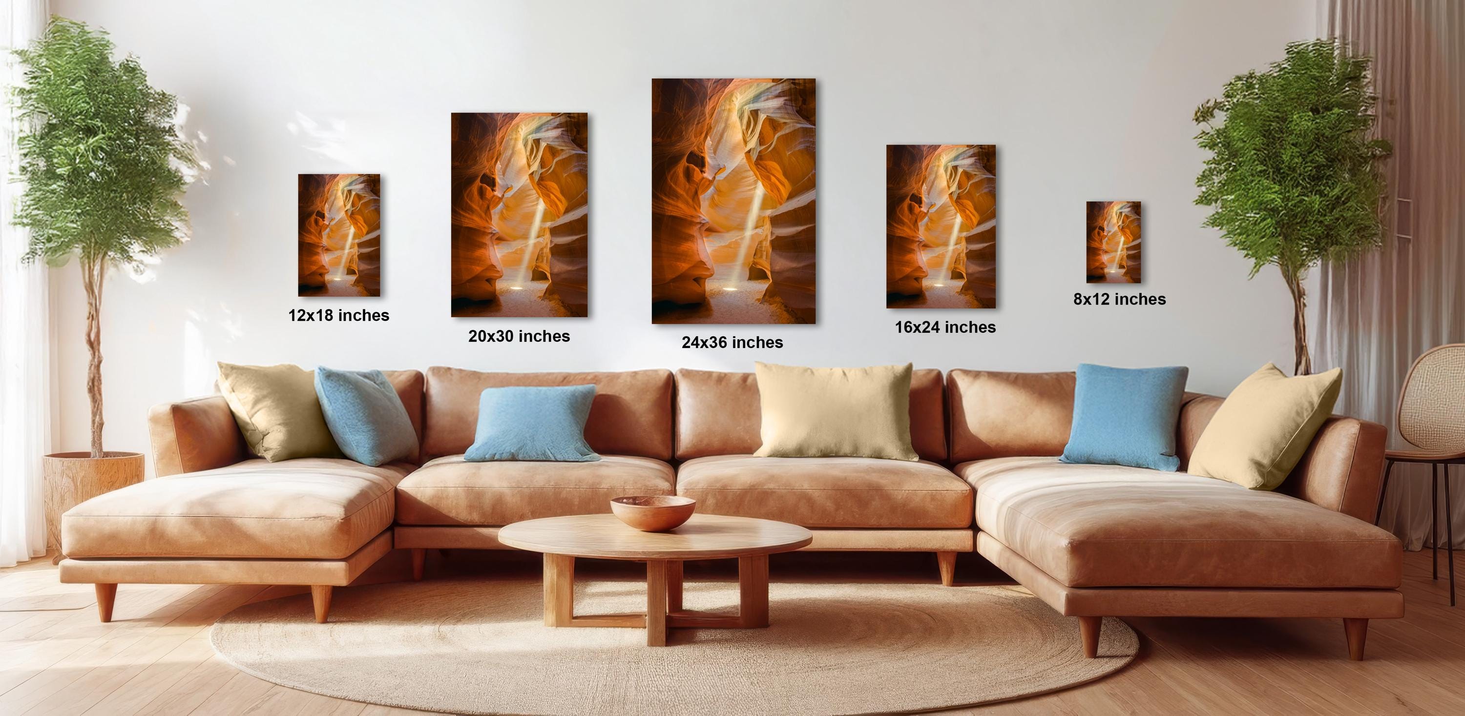 a modern living room with a large sectional sofa, a coffee table, and several potted plants. The sofa is positioned in front of a wall with four framed paintings of varying sizes, each depicting different scenes. The room has a warm and inviting atmosphere, with the natural light coming in from the windows.