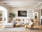 The image is a spacious living room with a large sectional sofa, a coffee table, and a fireplace. The room is decorated with various plants and has a neutral color palette.