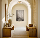 a hallway with a wooden floor, arched doorways, and a large painting of a forest scene hanging on the wall. There are two wooden benches on either side of the hallway, and a vase with flowers is placed on one of the benches. The hallway has a warm, inviting atmosphere with natural elements and a sense of tranquility.