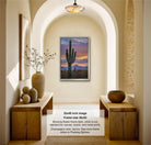 a framed photograph of a cactus against a sunset sky, hanging on a wall in a room with wooden furniture and decorative items.