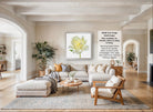 A modern living room with a large white sofa, a wooden coffee table, and a large framed print of a yellow flower on the wall.