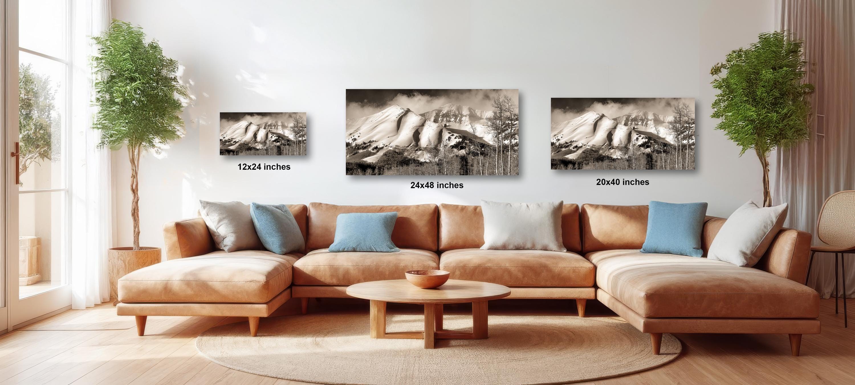 A modern living room with a large sectional sofa, a coffee table, and three framed black and white landscape photographs of mountains hanging on the wall.