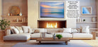 a cozy living room with a fireplace, white sofas, and a coffee table. The room has a warm and inviting atmosphere, with a fireplace providing a focal point and a large framed picture hanging on the wall.