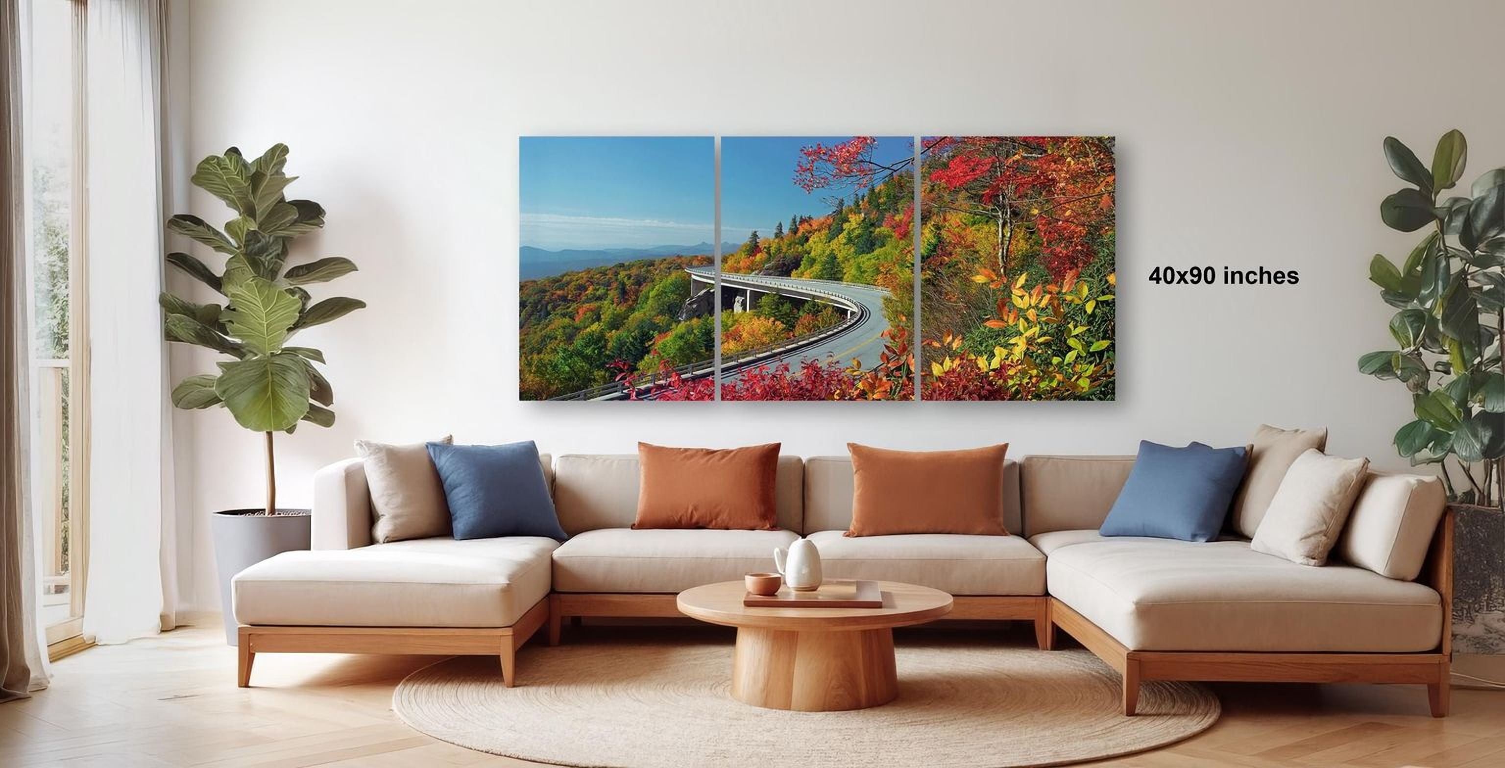 The image is a modern living room with a large, colorful painting of a scenic mountain landscape hanging on the wall. The painting features a winding road surrounded by trees and foliage in various shades of green, red, and orange. The room is furnished with a beige sofa and a wooden coffee table, creating a cozy and inviting atmosphere.