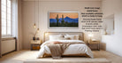 The image is a modern bedroom with a large bed, wooden furniture, and a framed desert landscape painting hanging on the wall.