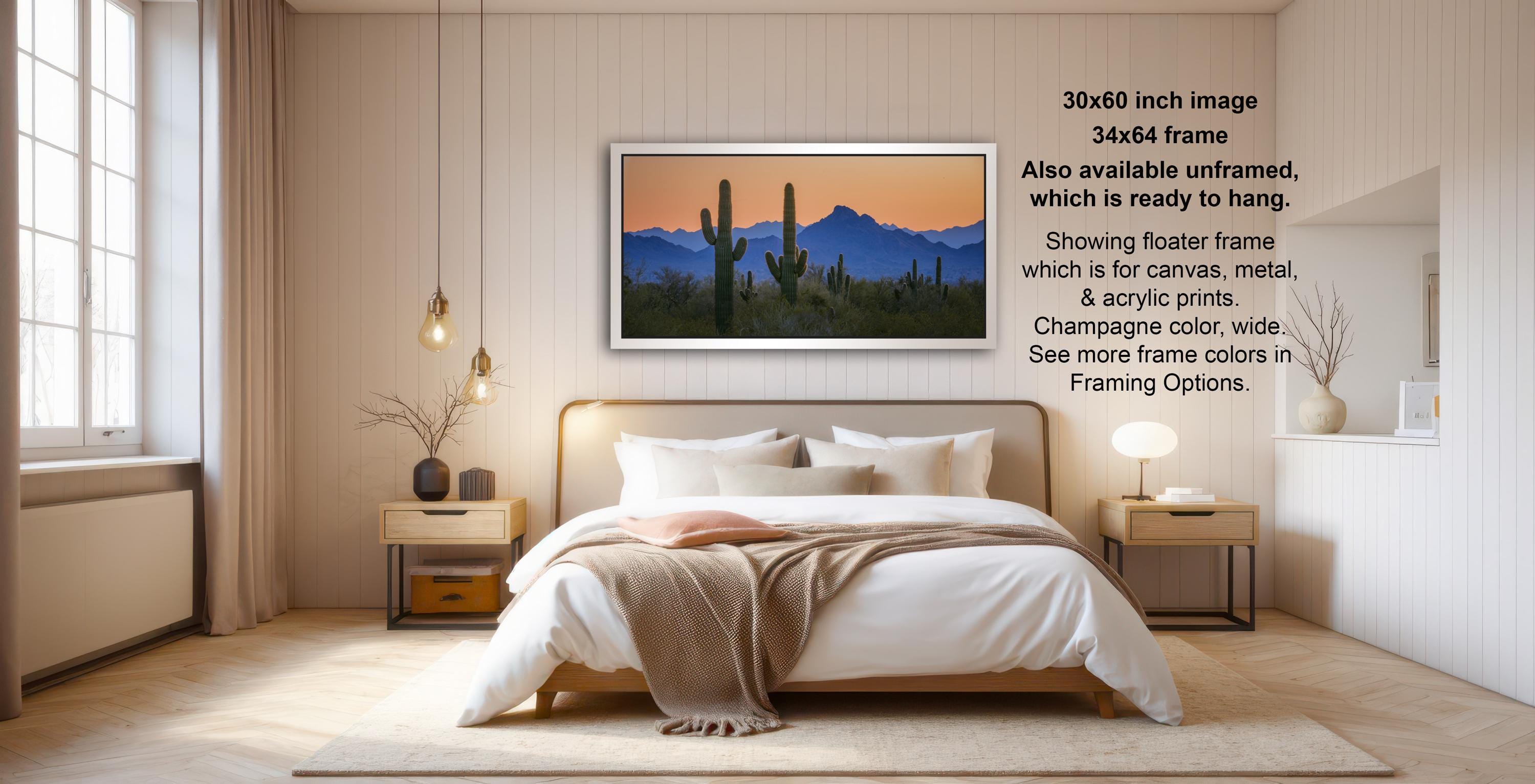 The image is a modern bedroom with a large bed, wooden furniture, and a framed desert landscape painting hanging on the wall.
