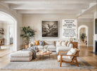 A spacious living room with a large sofa, a coffee table, and a fireplace. The room is decorated with various plants and has a neutral color palette.