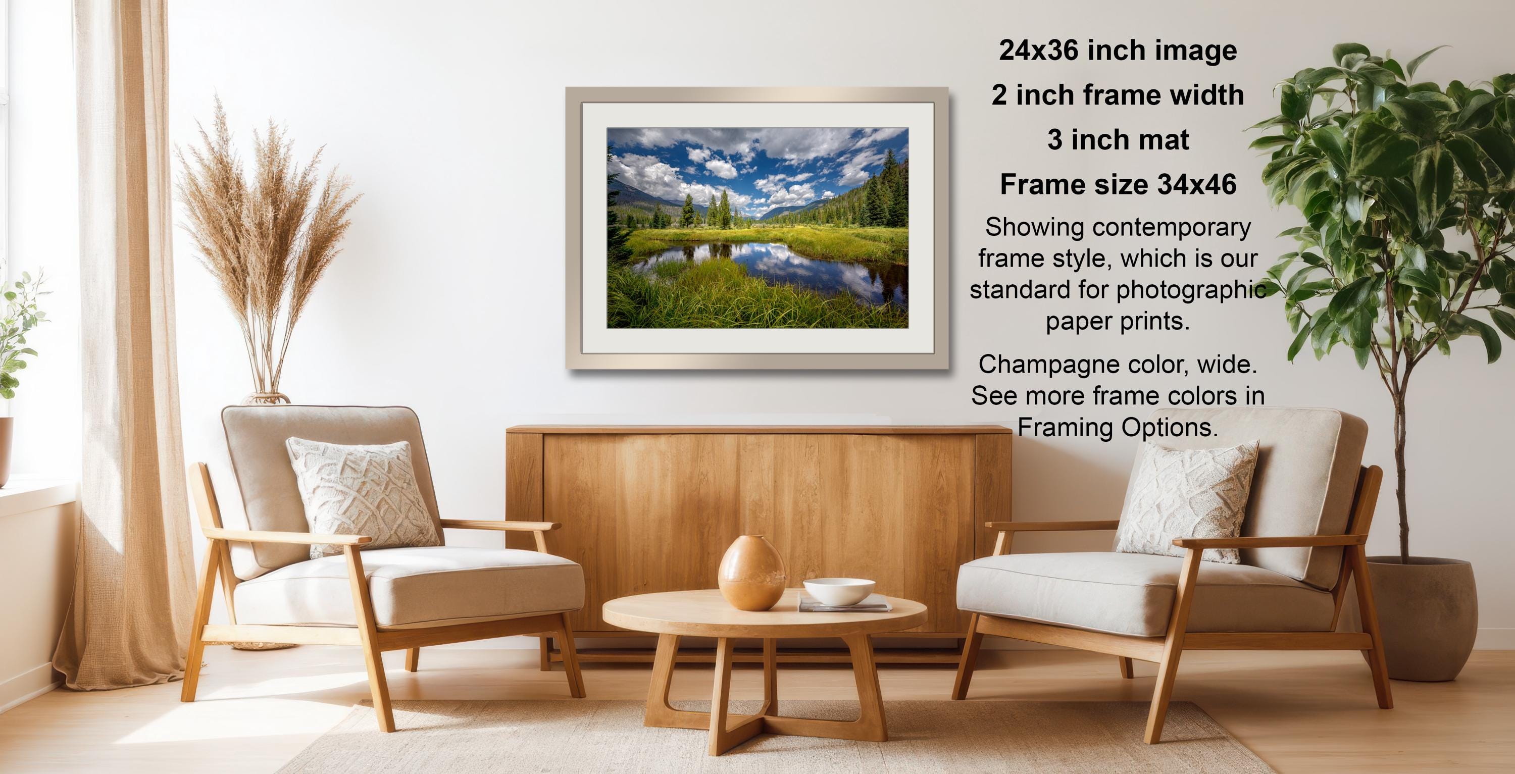 a living room with a wooden coffee table, two white armchairs, and a framed landscape photograph hanging on the wall.