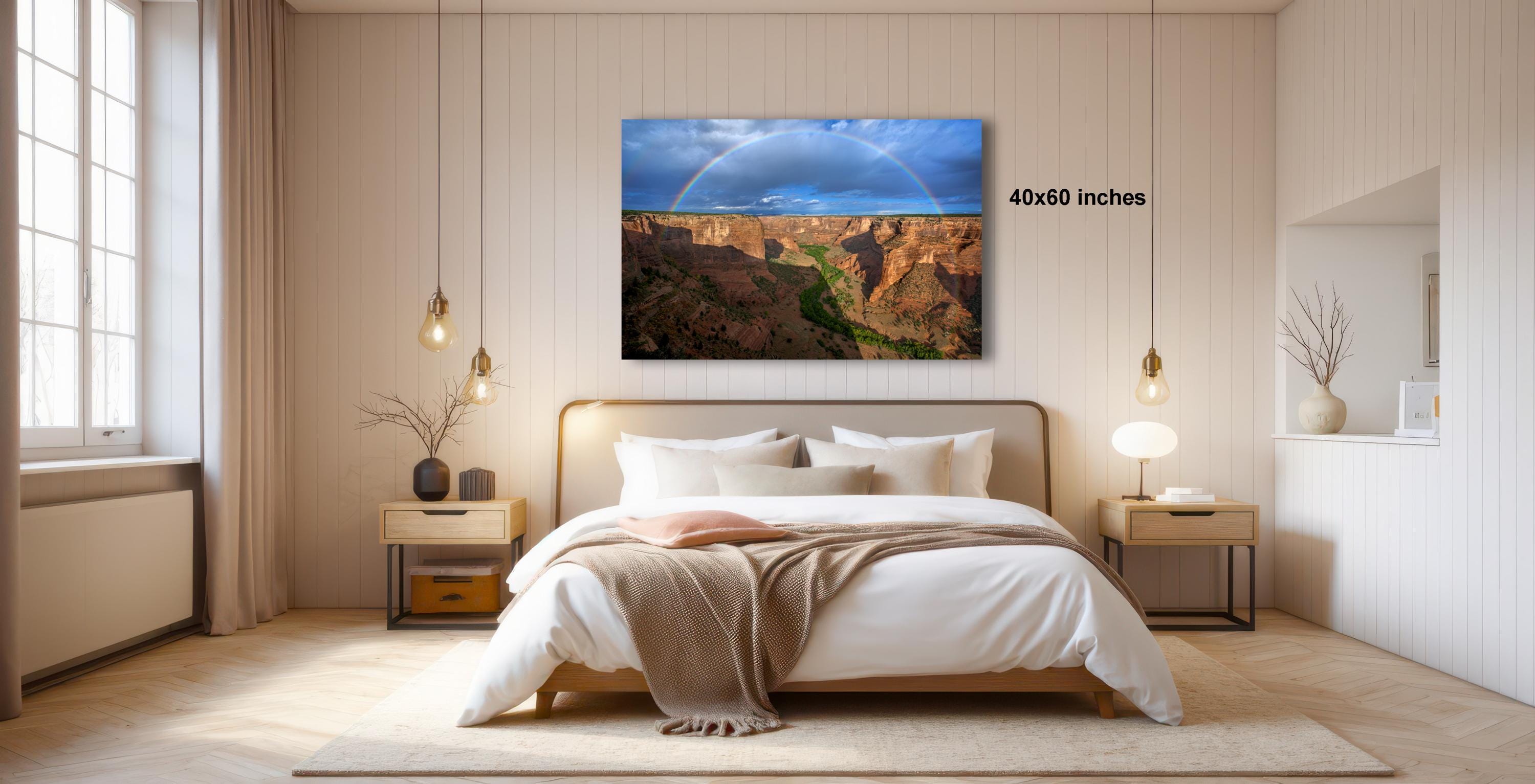 a serene bedroom with a large bed, wooden furniture, and a large window that allows natural light to fill the space. Above the bed, there is a framed photograph of a scenic landscape, featuring a rainbow and a canyon. The photograph is framed with the dimensions "4060 inches" and is hung on the wall, adding a touch of nature and beauty to the room.