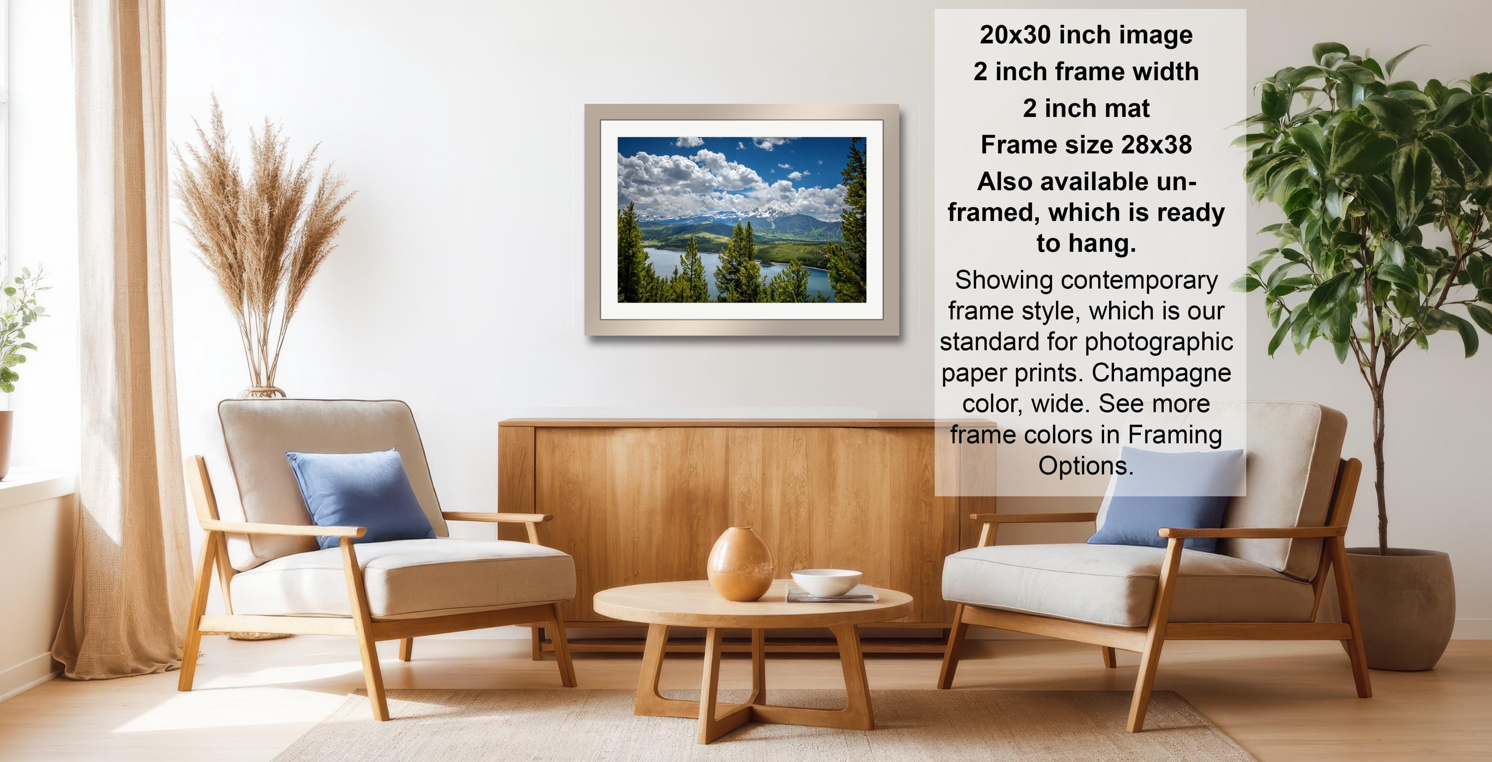 a living room with a framed landscape photograph hanging on the wall, a wooden coffee table in the center, and two armchairs facing each other.