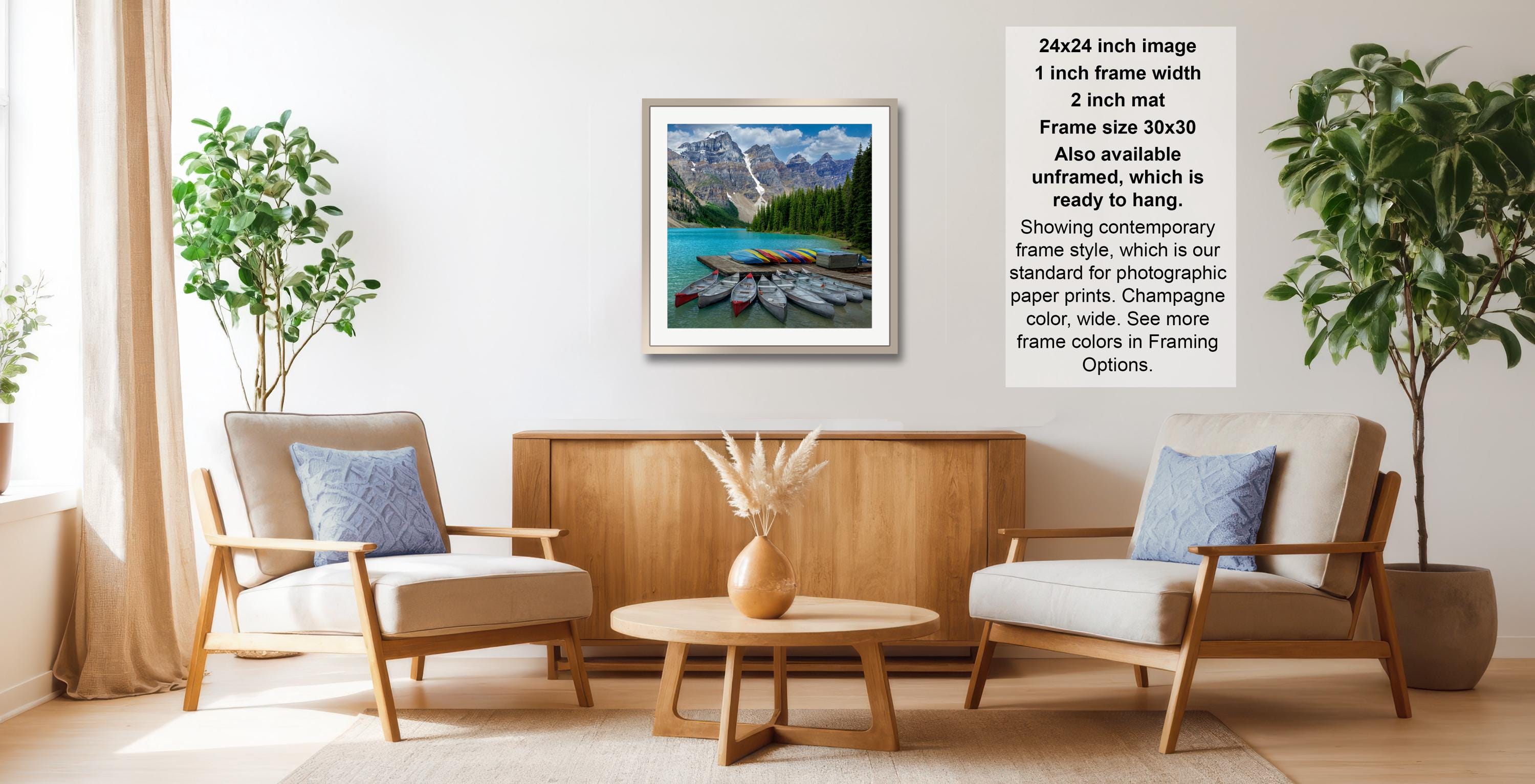 a modern living room with a wooden coffee table, two beige armchairs, and a framed landscape photograph hanging on the wall.