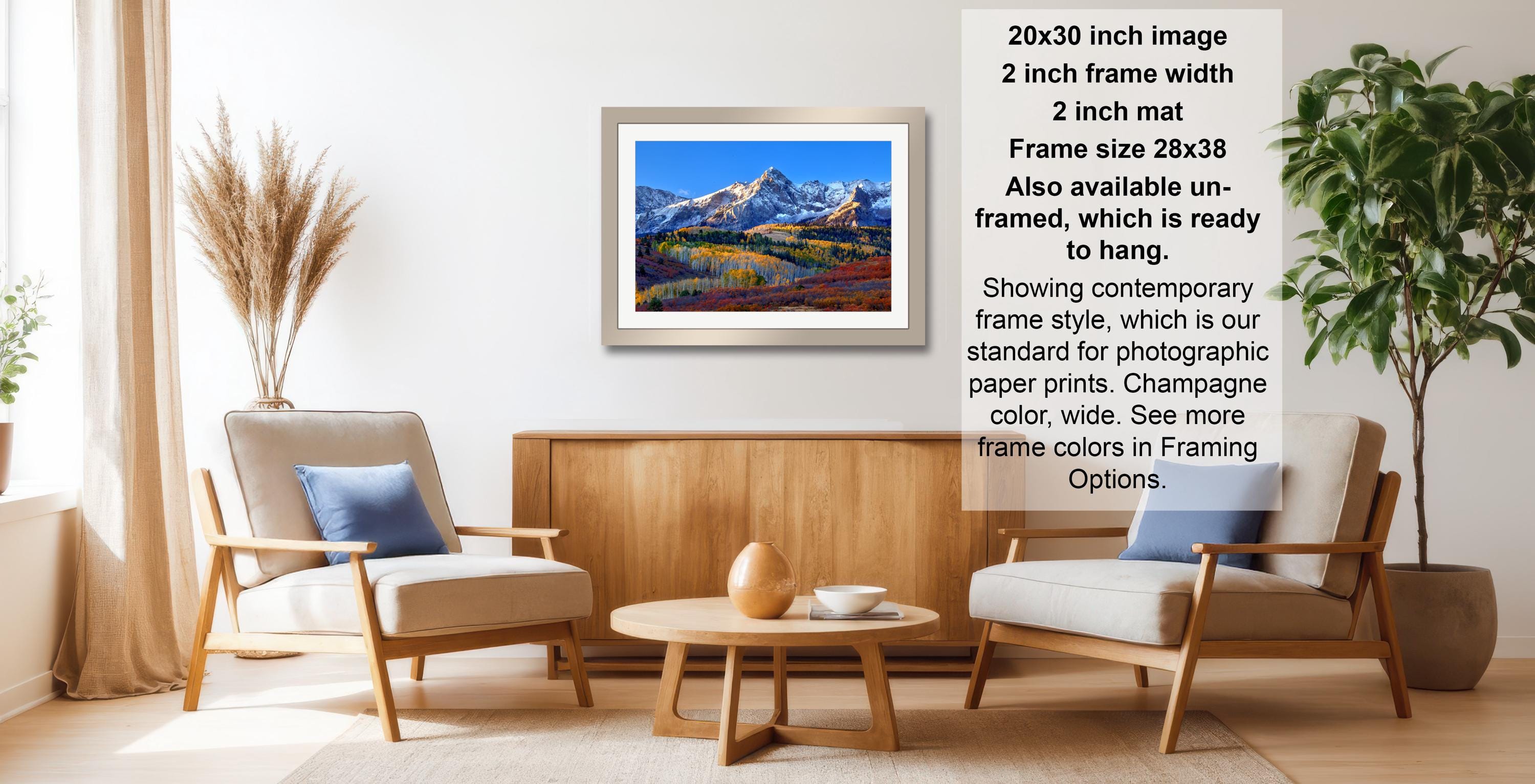 a living room with a framed landscape painting hanging on the wall, a wooden coffee table in the center, and two chairs facing each other.
