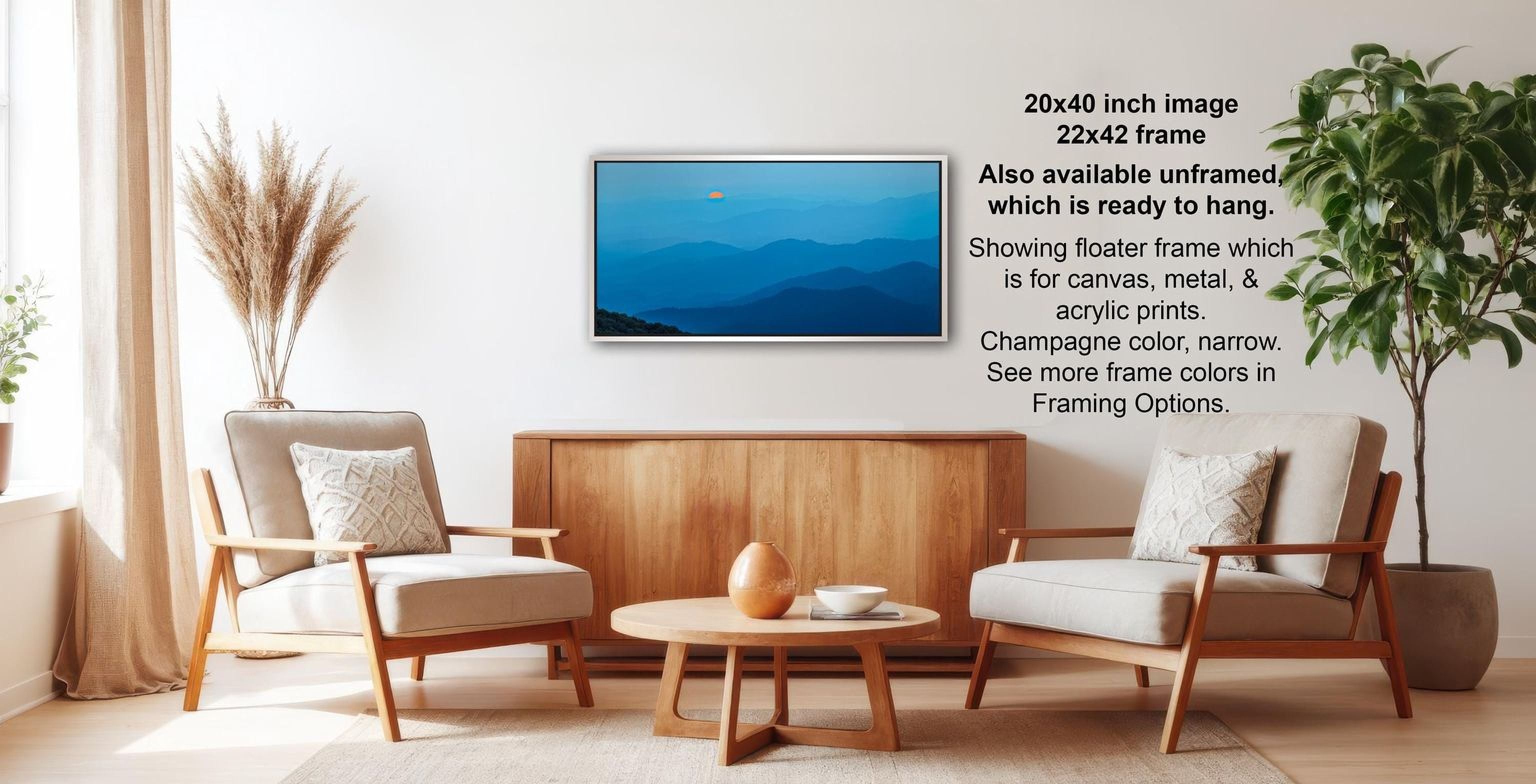 a living room with a wooden coffee table, two white armchairs, and a wooden sideboard. Above the coffee table is a framed picture of a mountain landscape. The room has a minimalist and modern design, with a large window providing natural light and a potted plant adding a touch of greenery.