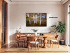 a serene dining room with a large wooden table surrounded by matching chairs. A painting of a forest scene with tall trees is displayed on the wall above the table. The painting is approximately 32x48 inches in size.