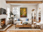 a cozy living room with a fireplace, a large framed picture of a forest path, and a comfortable white sofa with blue pillows.