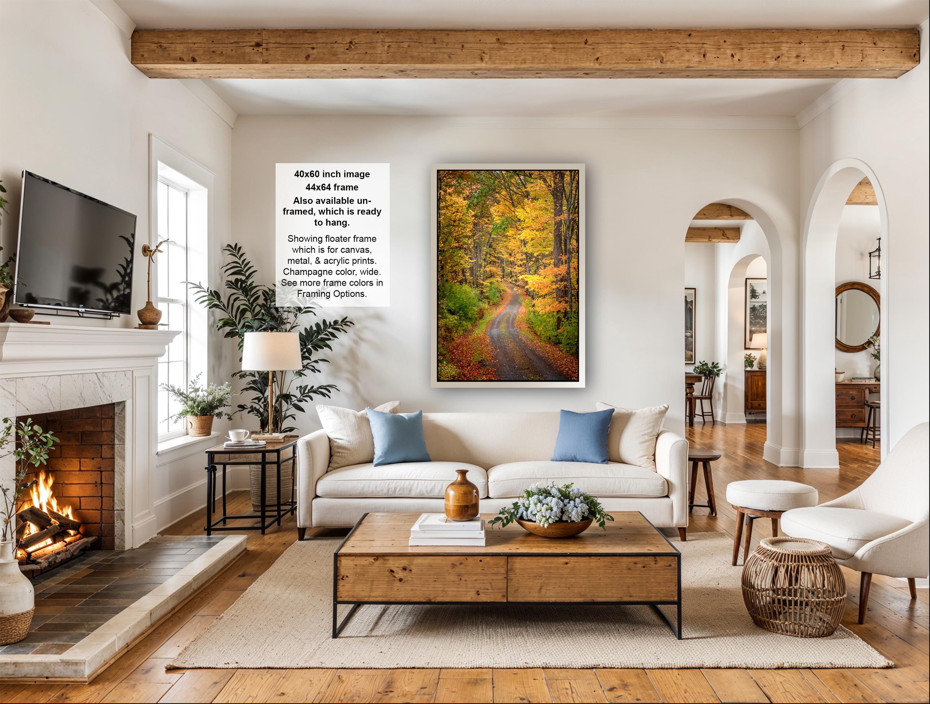 a cozy living room with a fireplace, a large framed picture of a forest path, and a comfortable white sofa with blue pillows.