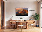 a large, framed photograph of a desert landscape with a mountain in the background, hanging on a wall above a wooden dining table with chairs.