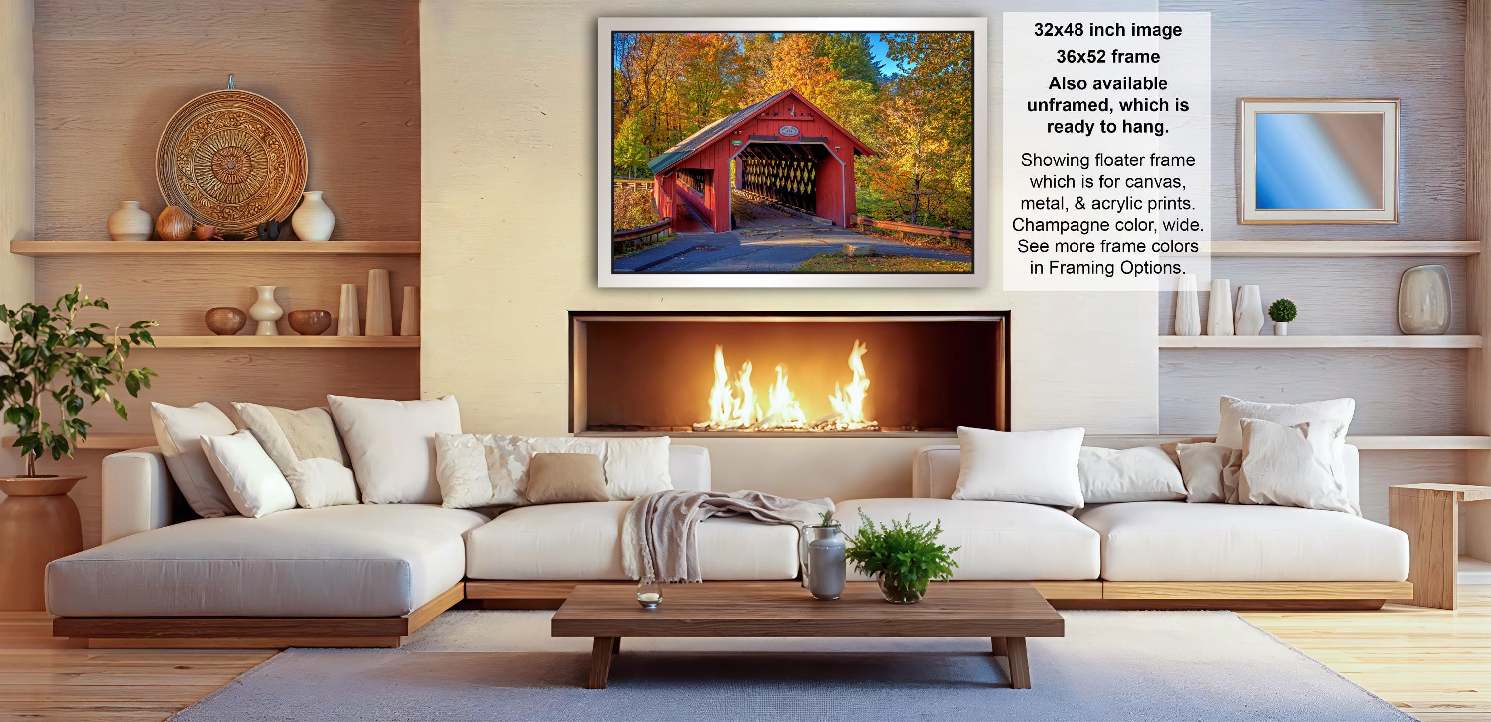 a cozy living room with a fireplace, white sofas, and a wooden coffee table. Above the fireplace, there is a framed image of a red wooden bridge with a covered walkway. The room also has shelves displaying various decorative items, such as vases and a potted plant.