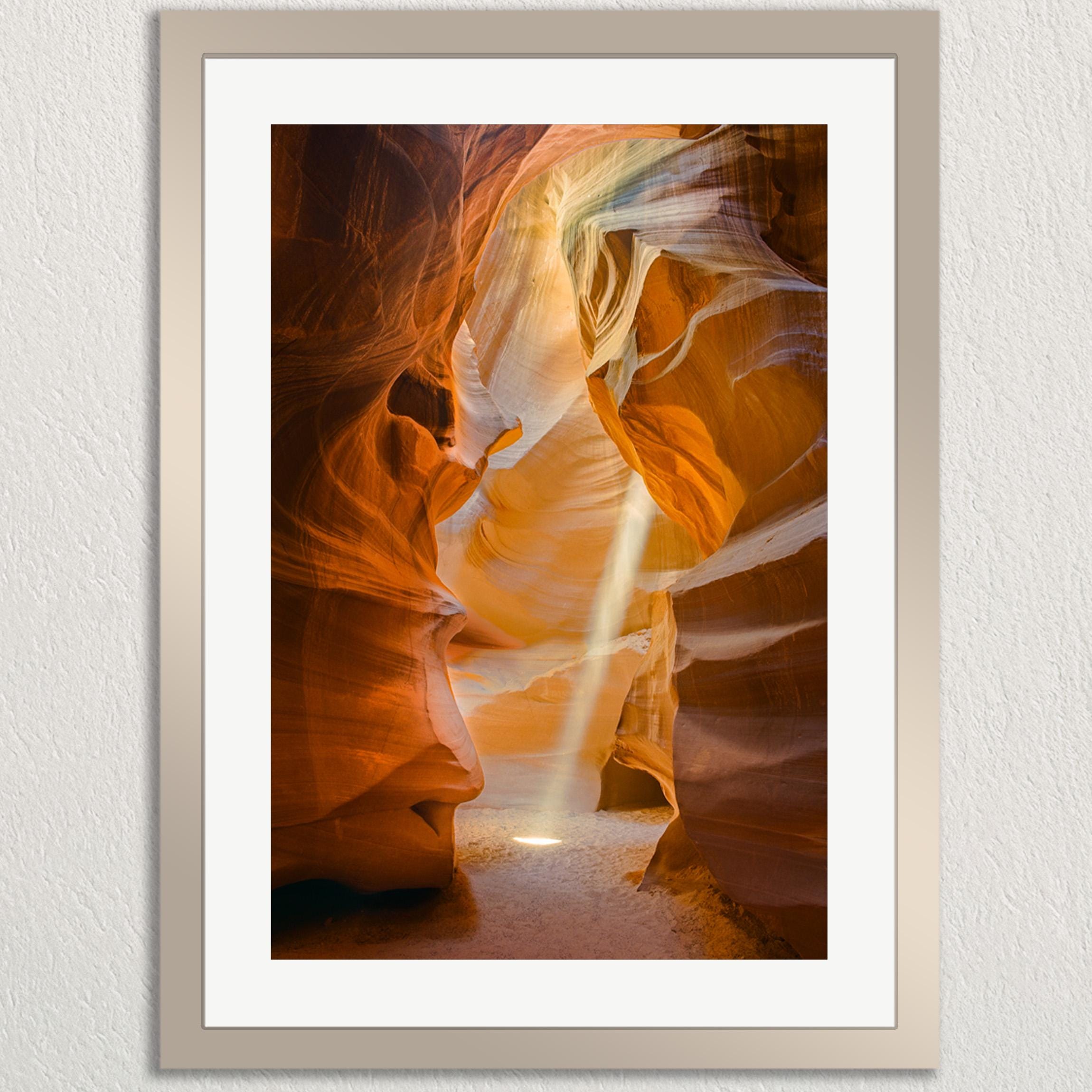 a stunning natural landscape with a narrow passage between two towering rock formations, creating a sense of depth and mystery. The sunlight filtering through the canyon walls casts a warm glow on the scene, highlighting the intricate patterns and textures of the rock formations. The image is framed and appears to be a piece of art, showcasing the beauty and grandeur of the canyon.