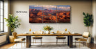 a large, three-panel landscape painting depicting a desert scene with mountains in the background. The painting is hung on a wall above a wooden dining table set with wine glasses, plates, and a vase of flowers.