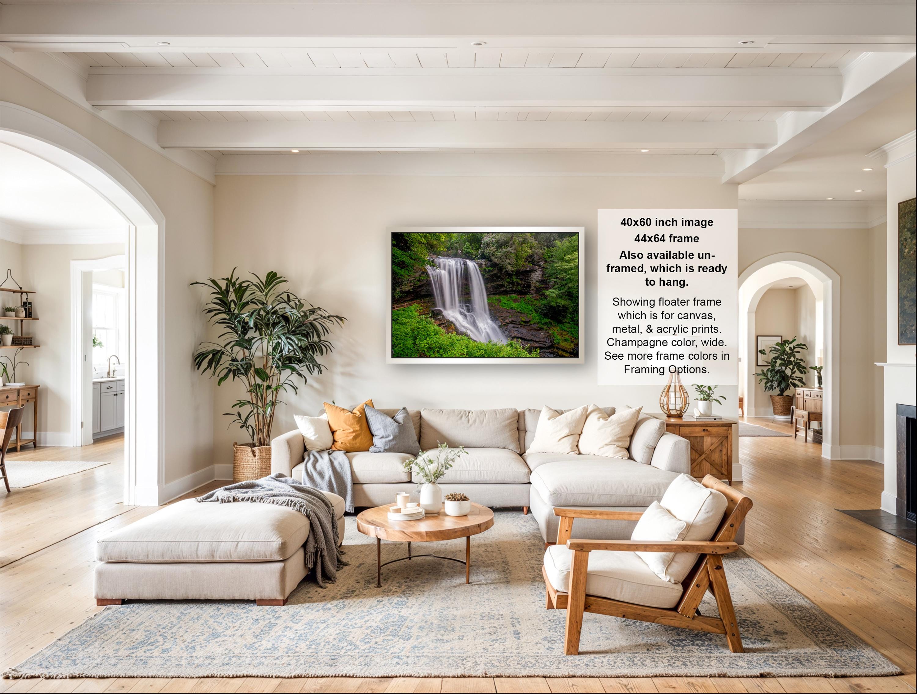 a large, white living room with a fireplace, a sofa, and a coffee table. There is a framed photograph of a waterfall hanging on the wall, and the room has a modern and minimalist design.