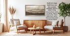 a living room with a wooden coffee table, two white armchairs, and a wooden sideboard. Above the coffee table is a framed landscape painting depicting mountains.
