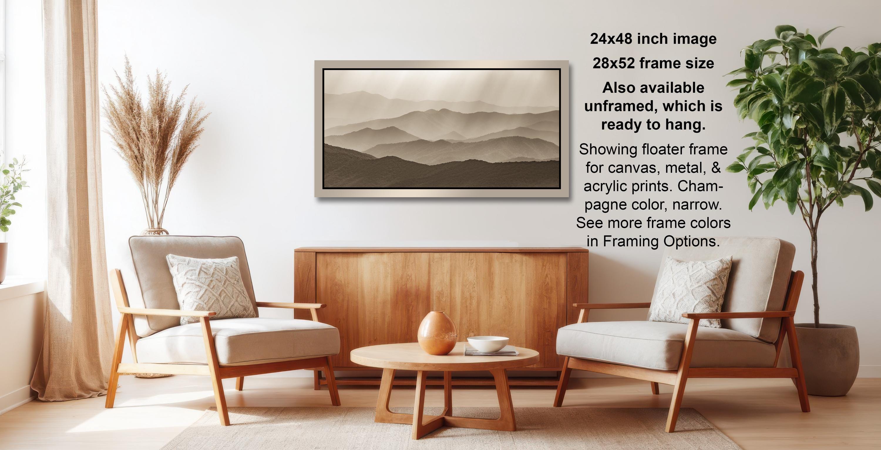 a living room with a wooden coffee table, two white armchairs, and a wooden sideboard. Above the coffee table is a framed landscape painting depicting mountains.