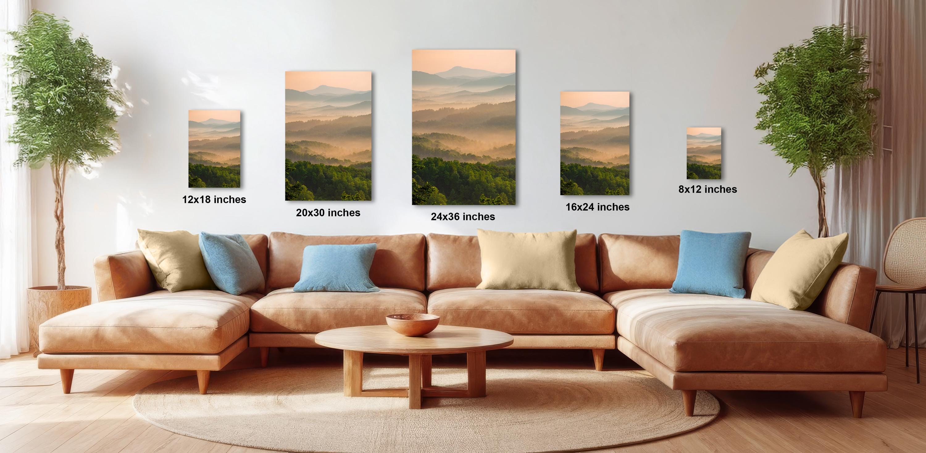 a large, brown sectional sofa with multiple pillows, a coffee table, and a potted plant in a living room setting. The sofa is positioned in front of a wall with four framed landscape paintings of varying sizes, each depicting a mountain scene. The paintings are arranged in a row, with the largest one being 24 inches wide and the smallest one being 16 inches wide.