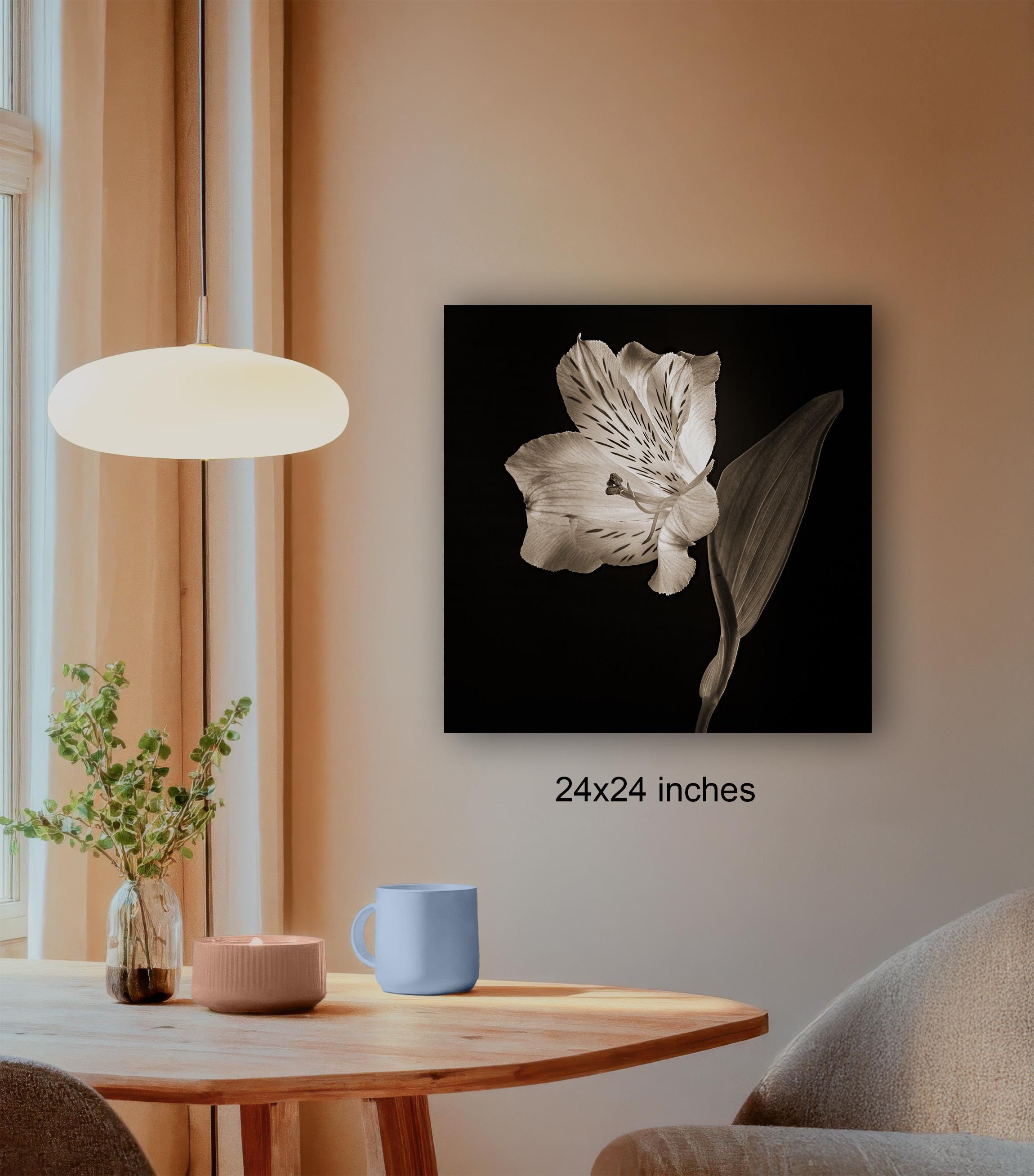 a wooden table with a blue mug, a candle, and a plant, set against a beige wall with a framed black and white photograph of a flower hanging on it.