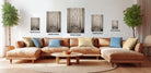 a modern living room with a large sectional sofa, a coffee table, and several potted plants. The walls are decorated with framed artwork depicting forest scenes, and the furniture is arranged to create a comfortable and inviting atmosphere.