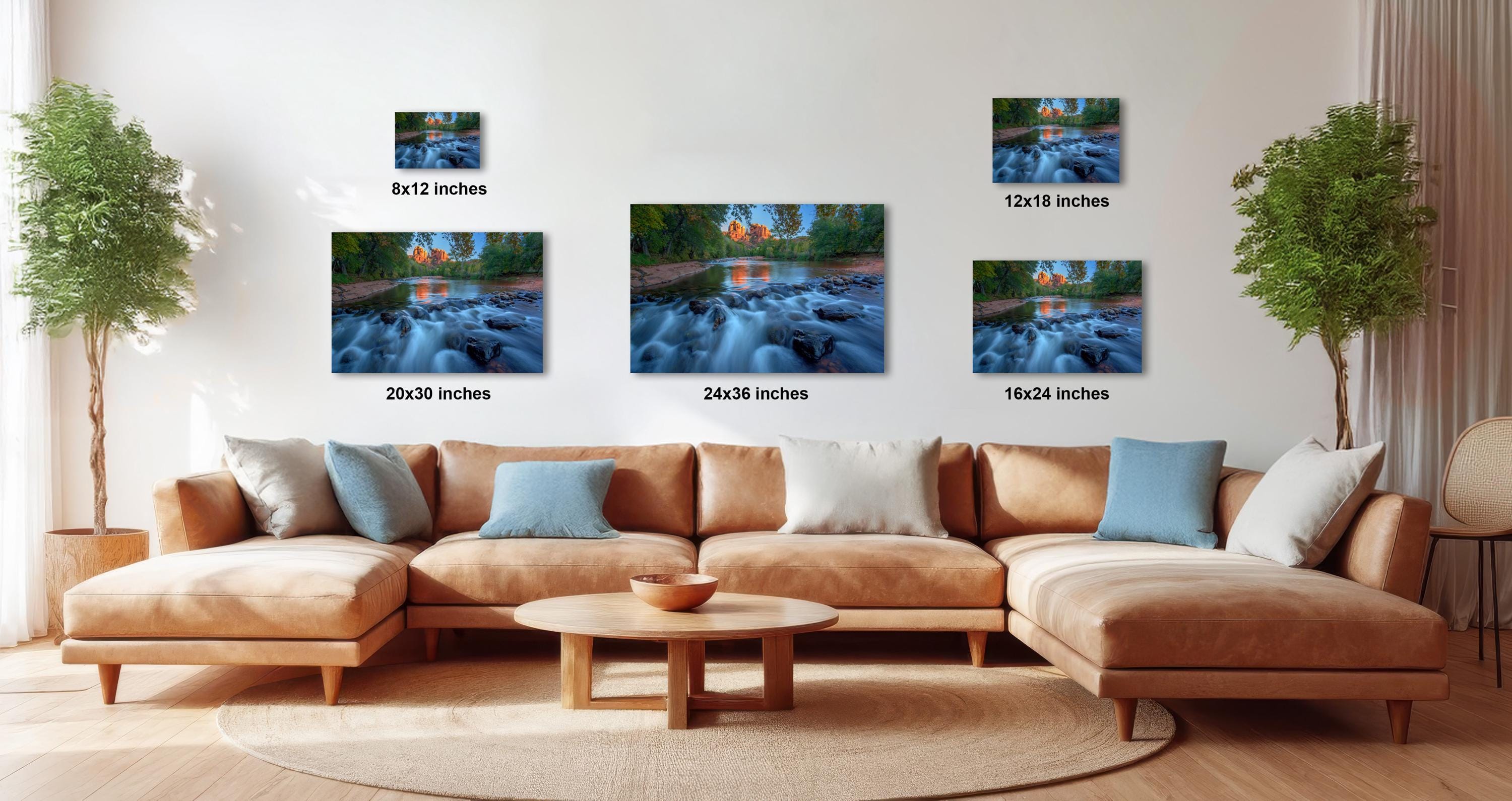 a living room with a large sectional sofa, a coffee table, and several potted plants. There are three framed photographs of a river scene displayed on the wall above the sofa. The photographs vary in size, with the largest one being 24 inches in height and the smallest one being 12 inches in height.