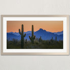 A framed photograph depicting a desert landscape with cacti silhouetted against a vibrant sunset sky.