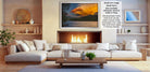 a cozy living room with a fireplace, white sofas, and a coffee table. The room has a warm and inviting atmosphere, with a large framed picture of a sunset over a lake hanging on the wall.