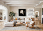 A modern living room with a large white sofa, a wooden coffee table, and a large framed black and white flower image on the wall.