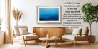 a living room with a framed landscape photograph hanging on the wall, a wooden coffee table in the center, and two white armchairs facing each other.