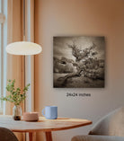 a wooden table with a blue mug, a candle, and a plant, set against a wall with a framed black and white photograph of a twisted tree.