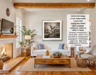 The image is a living room with a fireplace, a white sofa, a wooden coffee table, and a framed black and white photograph of a tree on the wall.