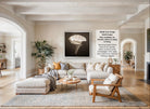 A modern living room with a large white sofa, a wooden coffee table, and a large framed black and white photograph of a flower hanging on the wall.
