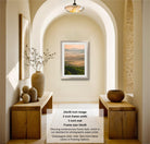 a hallway with a framed landscape photograph hanging on the wall, flanked by two wooden tables with decorative items on them. The photograph has a frame size of 24x36 inches and a 2-inch frame width, and it is displayed in a modern, contemporary style.