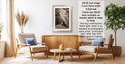 a living room with a framed photograph of a forest scene hanging on the wall. The room has two armchairs, a coffee table, and a potted plant, creating a cozy and inviting atmosphere.