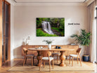 a serene indoor setting with a large framed photograph of a waterfall hanging on the wall. The photograph is surrounded by a wooden dining table and chairs, creating a cozy and inviting atmosphere.