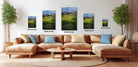 The image is a modern living room with a large sectional sofa, a coffee table, and several potted plants. The wall behind the sofa is decorated with four framed landscape photographs of varying sizes, each depicting a different scene. The photographs are arranged in a grid-like pattern, with the largest one at the top and the smallest at the bottom. The room has a warm and inviting atmosphere, with the furniture and decor complementing the natural elements of the landscape images.