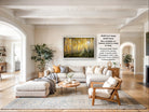 The image is a large, high-quality photograph of a living room with a large, framed painting of a forest scene hanging on the wall. The room has a neutral color scheme, with a beige sofa, a wooden coffee table, and a fireplace. The painting is framed in a white frame and is ready to be hung on the wall.