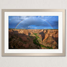 A framed photograph depicting a stunning canyon landscape with a vibrant rainbow arching across the sky above the rugged, rocky terrain.